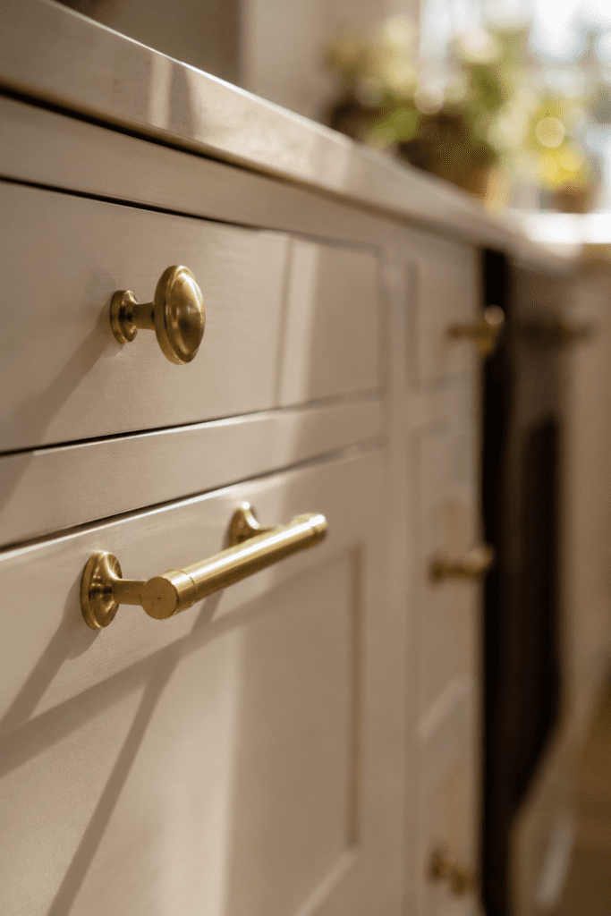 Brass kitchen cabinet hardware on cream cabinets with warm natural lighting.